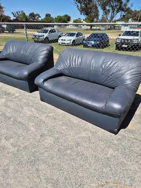 A pair of dark leather lounges set out on the grass.