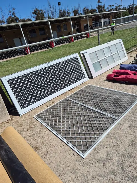 Aluminium security screen doors and a mesh gate leaning against a fence.